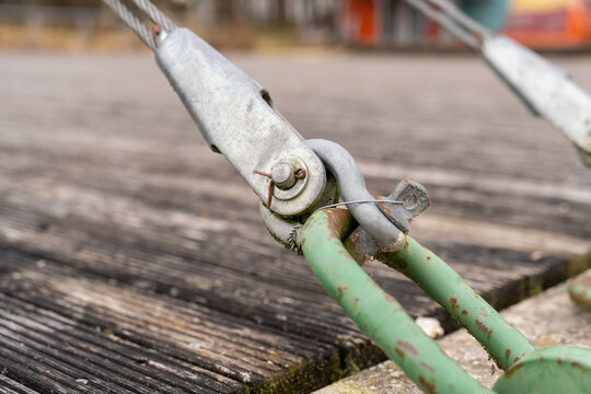 Weathered steel cable, thimble, and shackle system connecting to a green metal loop outdoors