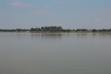 Tranquil Waters of a Southeast Asian River Flowing Past a Lush Tropical Shoreline with Village Houses.