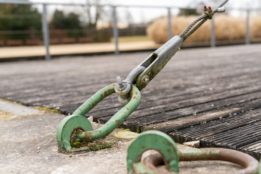 Industrial turnbuckle and wire rope tensioning a structure on a weathered wooden and concrete surface outdoors