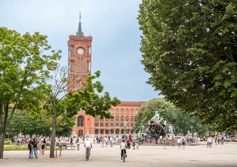 Berlin, germany, august 11, 2023. Rotes rathaus, the historic berlin city hall, and the illuminated neptune fountain attracting crowds in a lively city square