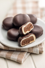 Dark chocolate truffles in the shape of coffee beans on plate on white table.