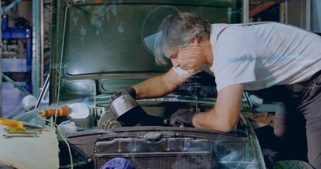 Leaning mechanic in white tee and suspenders pouring oil from metal can into engine bay, tools