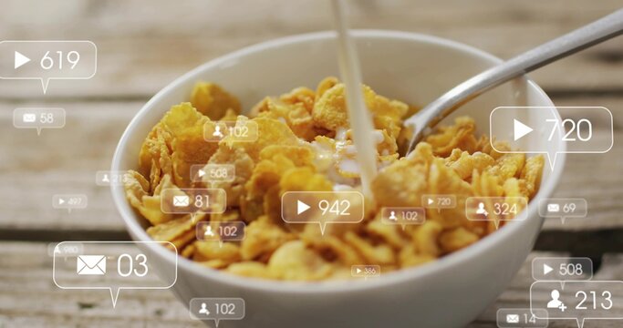 Pouring milk into white bowl of cornflakes on worn wooden table, spoon, social overlays floating