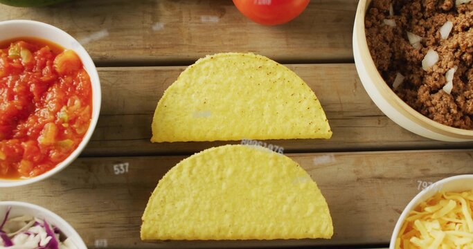 Displaying two yellow hard corn taco shells on rustic tabletop, with salsa, beef, cheese, cabbage
