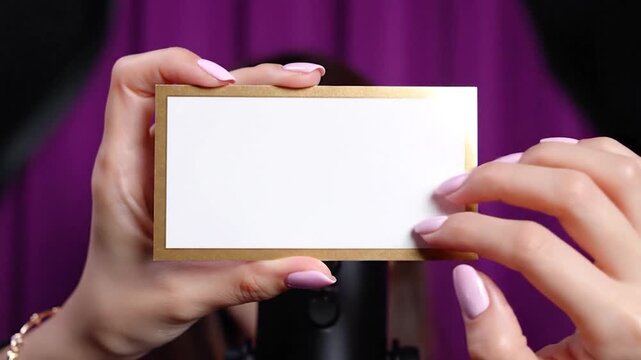 Hands holding a white card with a gold border, pink nails