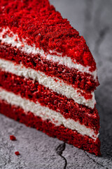 Slice of vibrant red velvet cake with cream cheese layers on a textured gray background
