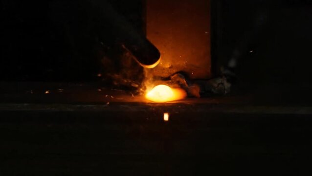 Molten metal being poured into a mold in an industrial setting viewed from the side