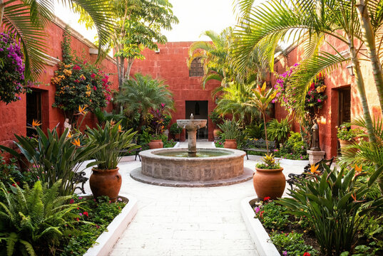 Peaceful colonial courtyard with a central stone fountain and vibrant tropical plants surrounded by deep red volcanic sillar walls in Arequipa, Peru