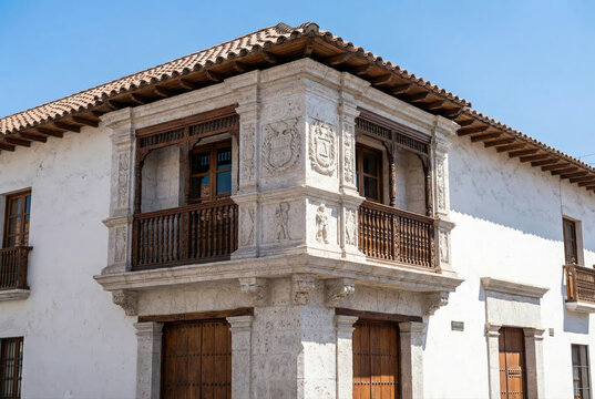 Ornate colonial corner balcony made of carved sillar stone and dark wood on a historic white building under a clear blue sky in Arequipa, Peru