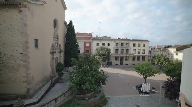 A peaceful wide view of La Garriga town hall and square with trees and historic buildings under a bright sky