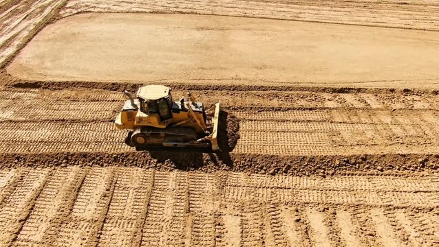 Aerial view of a bulldozer working on a large dirt field with rows of tilled soil