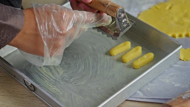 Close up of muslim hand Making Kaastengels cookies by cutting dough into rectangles on metal pan