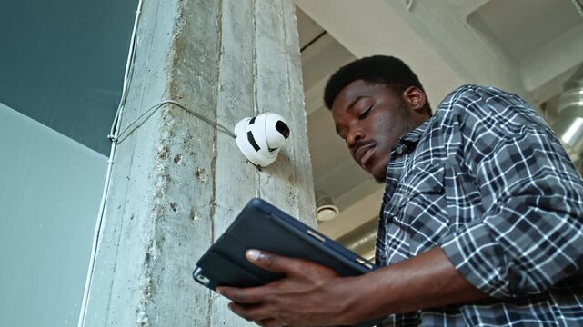 Worker inspects security camera on wall in modern office setting during daylight hours