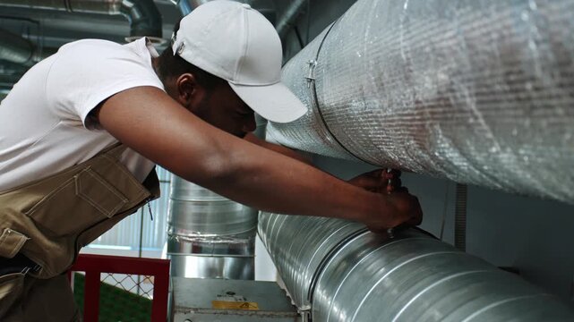 Worker installs ventilation duct in building during daylight hours