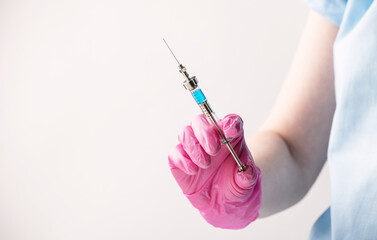 reusable glass syringe with blue medicine on a white background in the hands of a doctor. History of science and medicine, alchemy, vaccination