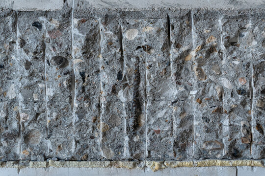 Close-up of jagged, chipped edge of gray concrete slab from construction. Reveals gravel aggregate, rebar, and chisel marks. Raw industrial texture, perfect as gritty building background.