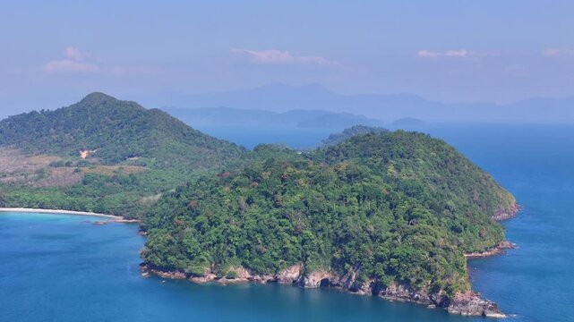 Aerial view of Koh Phayam coastline revealing turquoise bay, sandy beach, forested hills, and calm tropical sea under clear skies.