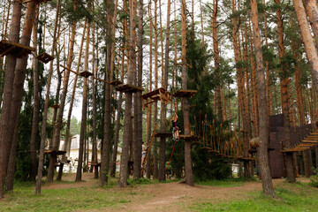 Obraz premium young toddler boy is riding a zip line in adventure nature activity park. continuous belay system on him. harness and safety line