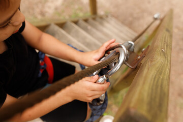 young toddler boy child is engaging with safety equipment on a ropes course in adventure nature activity park. continuous belay system on him. harness and safety line