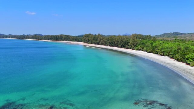 Aerial view of Koh Phayam beach, gentle waves, tropical trees, and calm turquoise sea on a sunny day.