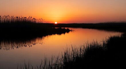 Obraz premium Serene Wetland Sunset with Calm Water Reflection and Orange Sky Glow