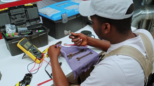 Man works on tools and repairs electronics in a workshop at midday