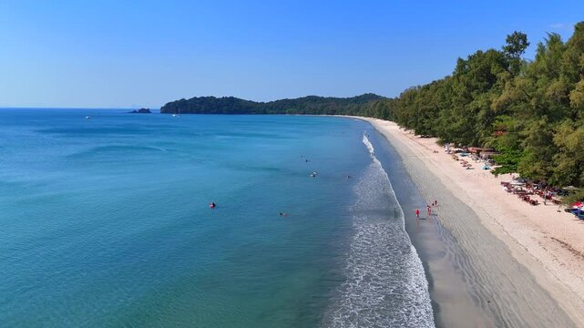 Aerial view of Koh Phayam beach, gentle waves, tropical trees, and calm turquoise sea on a sunny day.