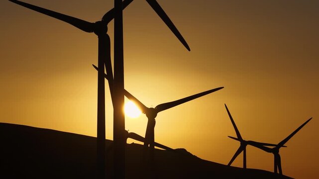 Aerial view of wind turbines silhouetted against a golden sunset, creating a stark contrast between the dark structures and the bright sky, Lanzarote, Spain.
