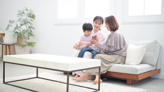 祖母と母と子どもが笑顔で抱き合う三世代家族、親子の幸せな動画　一緒にスマホを見る