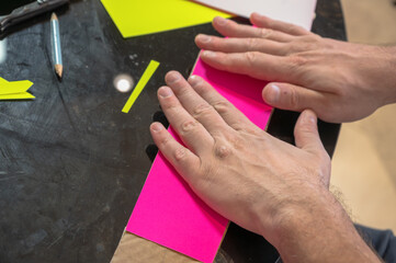 Close-up of hands crafting a cardboard sword on a table using cardboard, colored paper, and glue. DIY handmade project, creativity and imagination concept, eco-friendly hobby and recycled materials. 