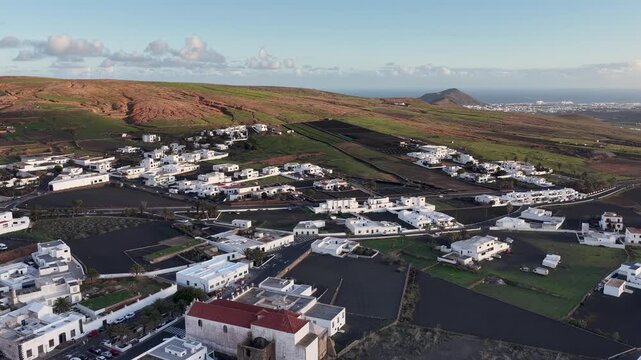 Aerial view of white buildings contrasting against the dark fields and green hillsides, creating a striking landscape, Teguise, Canary Islands, Spain.