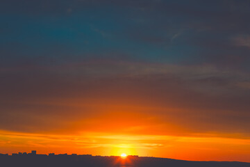 Obraz premium Sunset over distant cityscape. Buildings silhouettes contrast against the glowing horizon. Silhouette of a low-lying cityscape visible against the bright, fiery glow of setting sun