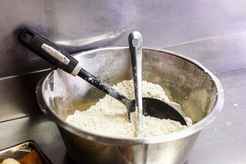 Fototapeta premium Metal bowl filled with white wheat flour and mixing spoons in a professional bakery kitchen for bread making.
