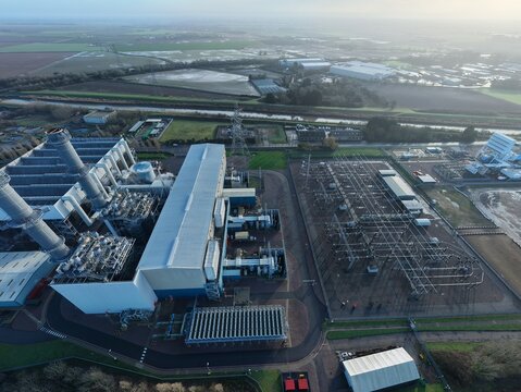 Aerial view of the industrial landscape, where the power station's angular structures contrast with the soft, green fields beyond, Spalding Power Station, Spalding, United Kingdom.