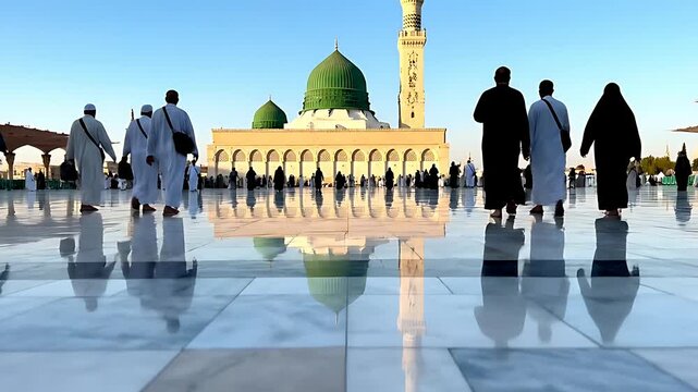 Pilgrims walk across a reflective marble courtyard toward the Prophet's Mosque featuring the iconic green dome and tall minaret