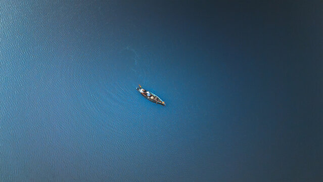 Aerial view of a lone boat cutting through the tranquil, deep blue waters, its wake a fleeting dance on the serene surface, Thanh pho Hoi An, Quang Nam, Vietnam.