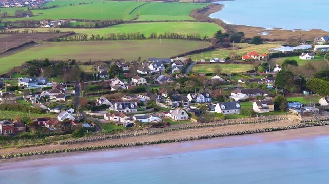 4K cinematic drone footage gliding over houses on Portrane Beach, surrounded by stacked tyres forming a sea defence_69