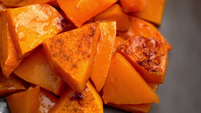 Close up of baked pumpkin slices coated with olive oil and seasoning in ceramic dish. Orange squash chunks