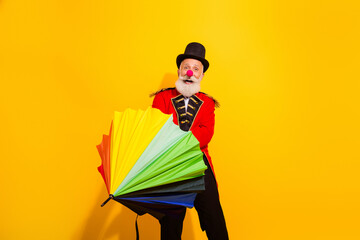 Colorful circus magician with rainbow umbrella performs joyful tricks against a bright yellow background creating festive mood © deagreez