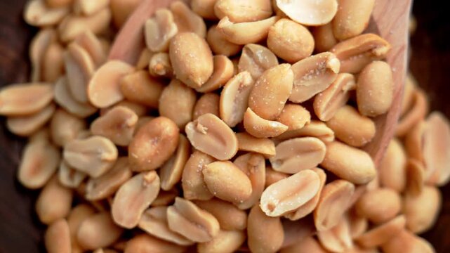 Top view of a pile of salted roasted peanuts inside a wooden bowl with spoon. Crispy snack. High protein legume food