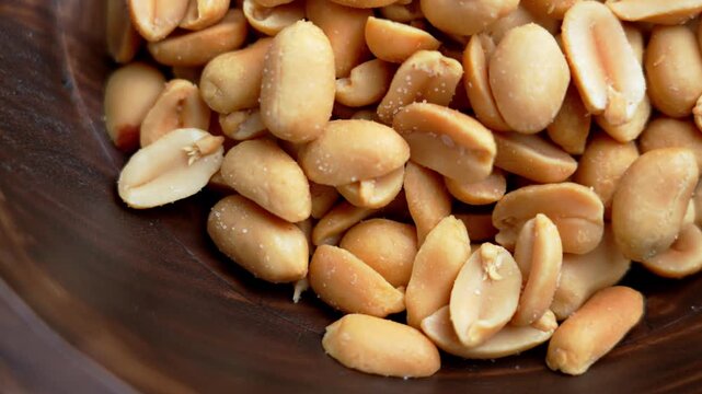 Roasted salted peanuts in a rustic wooden bowl. Top view. Rotation