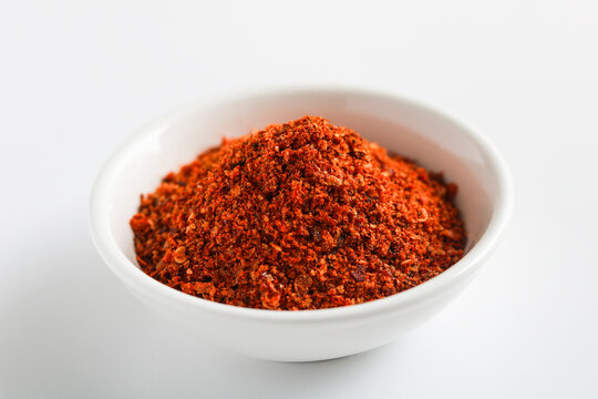 Spicy red chili powder in a white bowl isolated on a white background. A staple aromatic ingredient for Mexican, Indian, and Asian cooking presented in a clean, modern style.