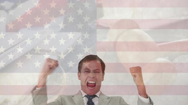 Businessman raising fists and starting celebrating, pumping arms under translucent US flag overlay