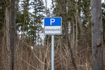 Fototapeta premium Parking sign reading “Abholpunkt” centered in frame, mounted on pole in forest environment. Pickup point sign with trees in background