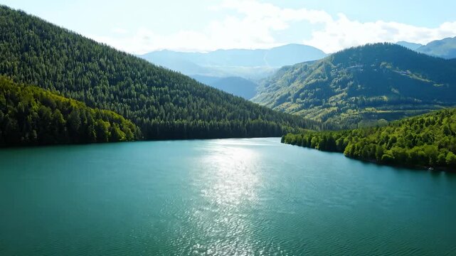 The tranquil lake reflects the lush green landscape surrounding it. Majestic mountains border the peaceful lake, emphasizing the natural beauty of this serene environment.