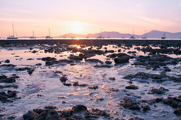 Obraz premium Serene Coastal Sunset Over Rocky Shoreline With Sailing Boats