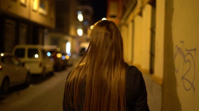 Woman walking alone on city street at night rear view