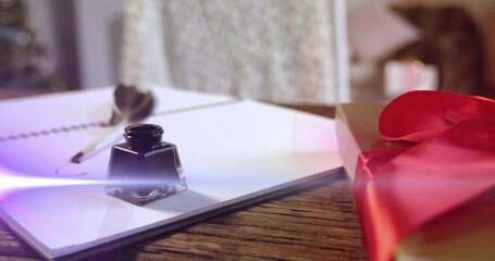 Sitting glass ink bottle on wooden table near window, with spiral notebook, quill, gift, flare