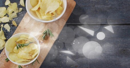 Showing two white bowls holding potato chips on cutting board at kitchen table with rosemary, salt © vectorfusionart