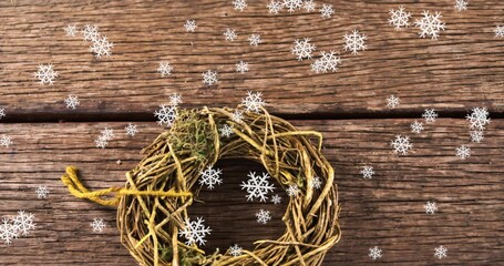 Naklejka premium Displaying grapevine wreath with moss and yellow twine on weathered planks, scattering snowflakes